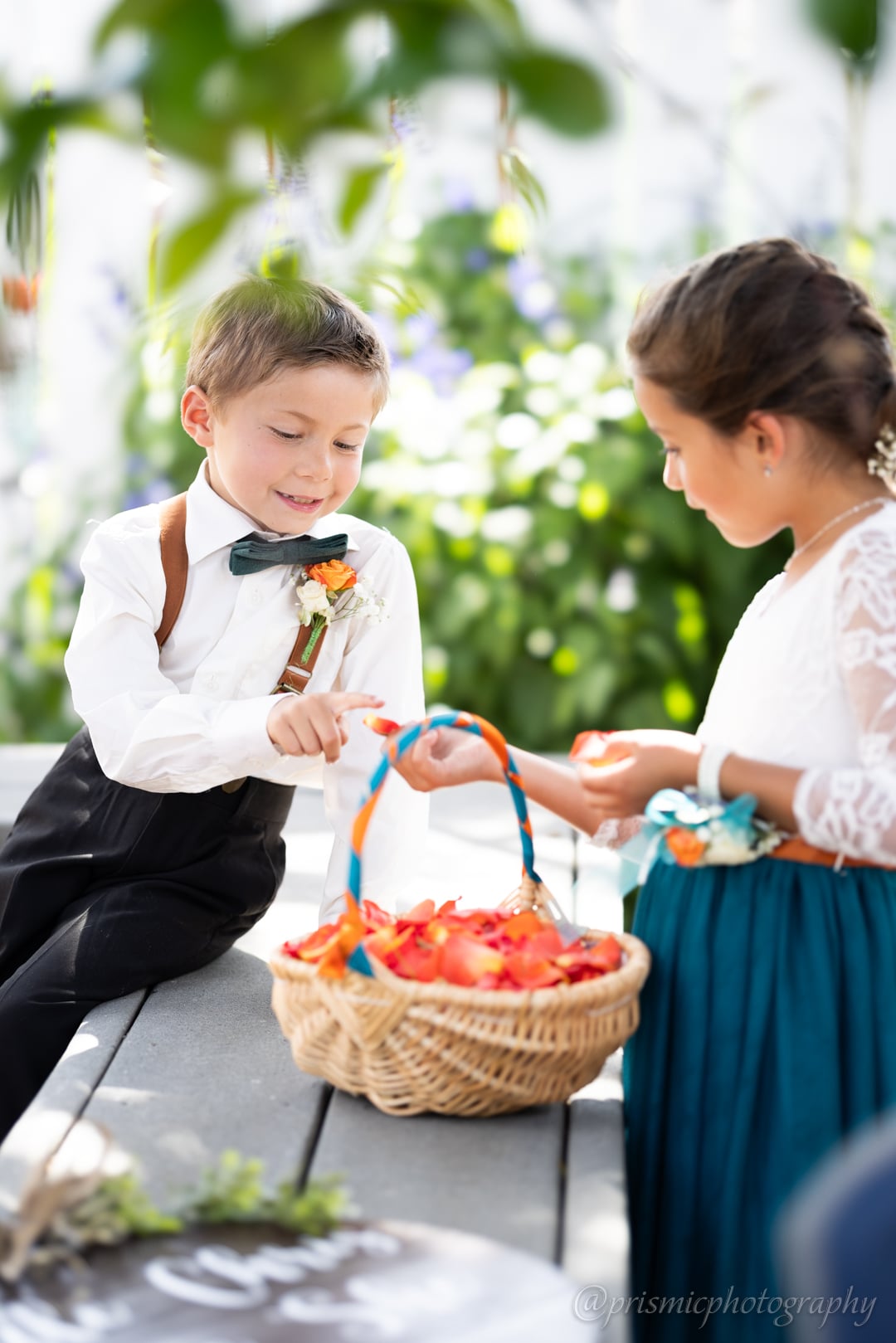 Formally dressed children trade flower petals on a bench at a wedding