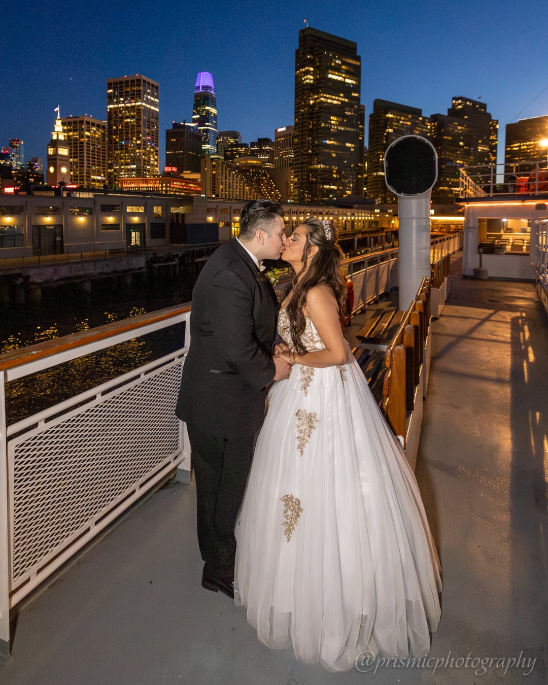 A couple kisses in front of a San Francisco backdrop on the Hornblower boat in SF.
